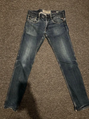 Replay anbass jeans - Snygga blå jeans från replay med smal passform och klassisk femficksdesign. Jeansen har slitningar och ljusare partier framtill för en trendig look. Tillverkade i bomull med detaljerade sömmar på bakfickan och läderpatch i midjan.