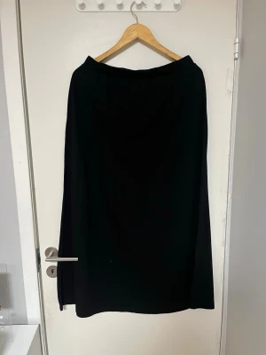 Svart lång kjol i enkel design - En svart lång kjol med rak passform och minimalistisk design. Kjolen har resår i midjan och är tillverkad i ett mjukt, följsamt tyg som ger ett snyggt fall. Perfekt för dig som gillar stilrena plagg.