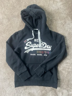 Superdry Hoodie - Säljer denna schyssta mörkblåa hoodien ifrån Superdry i storlek S/ xs med stor logga på bröstet och framsidan av tröjan. Alla defekter är visade i bilderna. Hör av dig om du har frågor. Priset är helt spikat i sten.