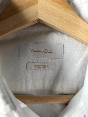 Vit skjorta från Massimo Dutti - Klassisk vit skjorta från Massimo Dutti i ett mjukt och svalt tyg. Skjortan har lång ärm, knappar framtill och en stilren krage. Perfekt för en clean och tidlös look. 