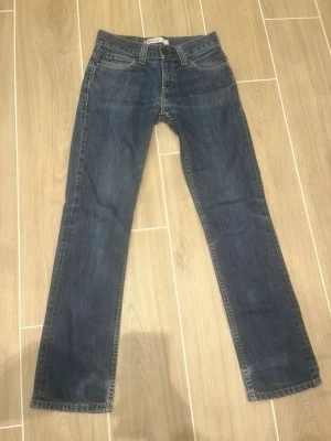 Blå raka jeans Levi's 511 Slim - Klassiska blå jeans från Levi's med rak passform och fem fickor. Jeansen har en mörk tvätt och är tillverkade i slitstark denim. Typisk Levi's-lapp bak i midjan och röd etikett på bakfickan. Perfekta för en avslappnad och tidlös stil.