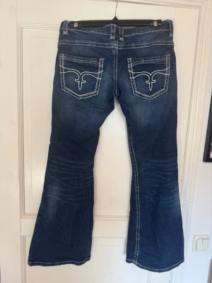 bootcut jeans - Säljer ett par mörkblå bootcut jeans. Jeansen har broderade bakfickor. Perfekta för dig som gillar en  trendig stil. Helt nya och aldrig använda. Det är Low Waits bootcut jeans. 