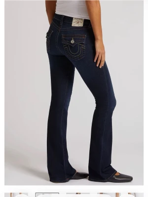 Mörkblå bootcut jeans från True Religion - Säljer mina snygga mörkblå bootcut jeans från True Religion med kontrastsömmar och ikoniska fickdetaljer bak. Säljer jeansen för att dom aldrig kom till användning. Jeansen har låg midja och klassisk femficksdesign. Tillverkade i bomull med en liten stretch för skön passform. Pris kan diskuteras och bilder kan skickas 💕