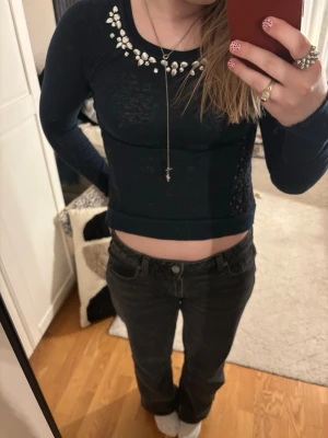 Mörkblå topp med spets och stenar från Hollister - Supersnygg mörkblå topp från Hollister med långa ärmar, spetsdetaljer på sidor och rygg samt glittriga stenar vid halsringningen. Perfekt för dig som vill sticka ut lite extra!