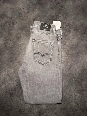 Grå jeans från Replay - Säljer ett par snygga grå jeans från Replay med klassisk femficksdesign och diskret tvättad look. Jeansen har normal passform och är tillverkade i bomull med en liten mängd stretch för extra komfort. Perfekta till alla dina outfits!