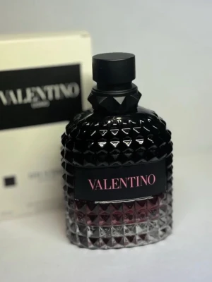 Valentino parfym med nitar - Snygg parfym från Valentino i en mörk, diamantmönstrad glasflaska med svarta och rosa detaljer. Flaskan har en cool nitdesign och svart lock, vilket ger en lyxig och edgy känsla. Perfekt för dig som gillar exklusiva dofter och stilren design.