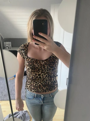 Leopardmönstrad croppad topp - Säljer en croppad topp med leopardmönster och korta ärmar. Toppen har en snygg, tight passform och en lätt rynkad detalj vid bysten. 