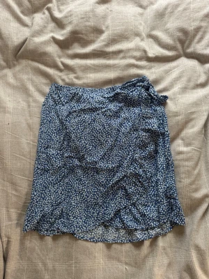 Blommig blå omlottkjol  - Söt blå kortkjol med vitt blommönster och omlottdetalj i midjan. Hör av dig vid frågor ❤️