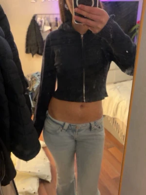 Svart croppad hoodie med dragkedja - Säljer en svart croppad hoodie med dragkedja framtill och huva. Hoodien har långa ärmar och en tight passform som ger en trendig look. Perfekt för dig som gillar streetwear och vill ha en enkel men snygg hoodie i garderoben.