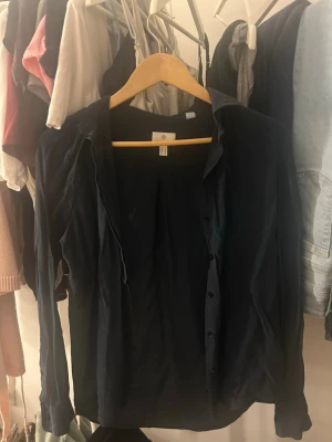 Mörkblå skjorta med knappar från gant  - Säljer en stilren mörkblå skjorta från gant med klassisk krage och knappar framtill. Skjortan har långärmad design och är tillverkad i ett lätt bomullsmaterial som passar perfekt till olika outfits. Enkel att matcha och ett måste i garderoben.