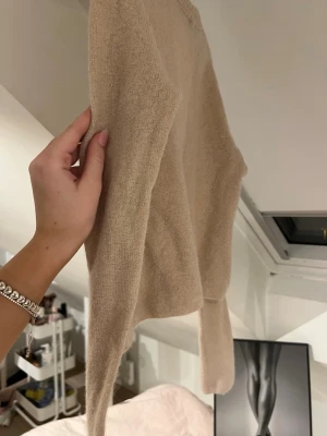 Beige kofta med knytband från Zara - Söt beige kofta med långa ärmar och tre dekorativa knytband framtill från Zara. Koftan är stickad i ett mjukt material och har en enkel, stilren design som passar perfekt till många olika outfits.