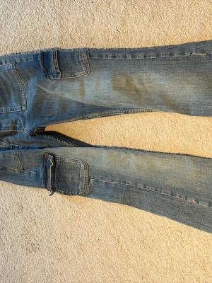 Blå cargobyxor i denim - Säljer ett par blå cargobyxor i denim med stora fickor på sidorna och klassisk cargomodell. Byxorna har en avslappnad passform och slitna detaljer för en cool, casual look. Perfekta för dig som gillar streetwear och praktiska fickor.