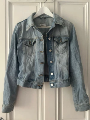 Ljusblå jeansjacka från Zoul - Ljusblå jeansjacka från Zoul med klassisk krage, bröstfickor med lock och knappstängning framtill. Jackan har långa ärmar och en rak, något kortare passform. Vintage.