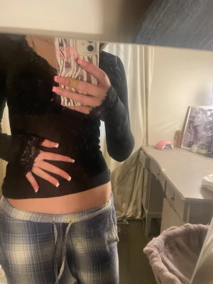 Svart långärmad topp med spets - Svart långärmad topp från Bik Bok med djup v-ringning dekorerad med spetsdetaljer. Tunn och mjuk i materialet, perfekt att styla med jeans eller kjol. Enkel och stilren design med en feminin touch tack vare spetsen vid halsen.