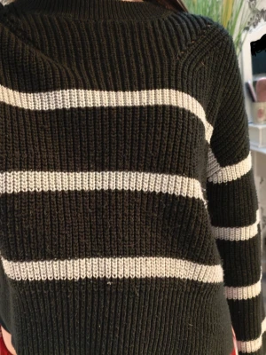 Svart stickad tröja med vita ränder - Säljer en svart stickad tröja med breda vita horisontella ränder. Tröjan har ribbstickade muddar vid ärmslut och nederkant samt en klassisk rund halsringning. Det finns även ett snitt på sidan av nederkanten. Perfekt för en avslappnad look