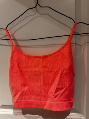 Ribbad korallfärgad linnetopp - Snygg ribbad linnetopp i en stark korallrosa färg. Toppen har smala axelband och croppad passform, perfekt till sommaren. Materialet är mjukt och stretchigt, vilket gör den bekväm att bära hela dagen.