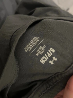 Grå Under Armour t-shirt - Snygg grå t-shirt från Under Armour med stort logotryck i svart och vitt på framsidan. Tillverkad i mjuk bomullsmix som känns skön mot huden. Perfekt för dig som gillar sportig och avslappnad stil.