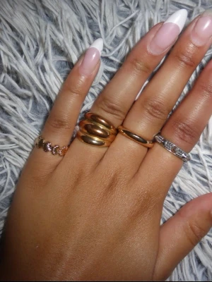 Mixade ringar i guld och silver - Säljer ett set med fyra ringar i olika stilar. Två ringar är i guldton, varav en är chunky och en är slät. En ring är i silverfärg med små stenar och en är tunn med pärldetaljer. Perfekt för dig som gillar att mixa metaller och skapa en personlig look.💗🍾🙌🏽