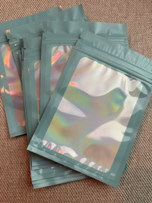 Holografiska zip-påsar - Säljer 20 stycken  holografiska zip-påsar i plast med förslutning. Ena sidan är helt holografisk och andra sidan är matt grå. Perfekta för förvaring av småsaker, smycken eller presenter. Storlek: 15x10cm 