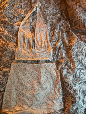 Topp + Kjol  - Söt halterneck topp med småblommigt mönster och knyt i nacken. Toppen är ärmlös och croppad, perfekt för varma dagar med matchande kjol till 