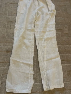 Vita linnebyxor med resårmidja - Säljer ett par klassiska vita linnebyxor med rak passform och resår i midjan. Byxorna är tillverkade i svalt linnematerial och har en enkel, stilren look som passar perfekt till sommaren. Inga synliga fickor eller detaljer.