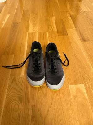 Svarta sneakers med gula detaljer - Snygga svarta sneakers med mesh-ovandel, svarta skosnören och vit sula med gula detaljer undertill. Skorna har en sportig look och är låga i modellen. Perfekta för dig som gillar en stilren men ändå färgglad touch på dina sneakers.