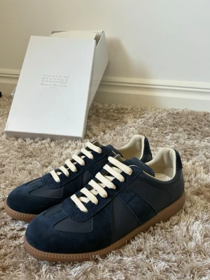 Mörkblå  Maison Margiela - Snygga marinblå sneakers från Maison Margiela med ovandel i mocka och läder, vita snören och klassisk gummisula. Skorna har en låg profil och stilren design som passar perfekt till streetwear eller casual outfits.