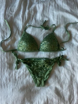Grön glittrig bikini från Calzedonia - Snygg grön bikini från Calzedonia med glittriga paljetter på både överdel och underdel. Klassisk trekantsmodell med knyt i sidorna och i nacken. Helt oanvänd och säljs inte längre. Skulle säga att den passar S/M i nederdel och B/C-kupa upptill🩷🩷