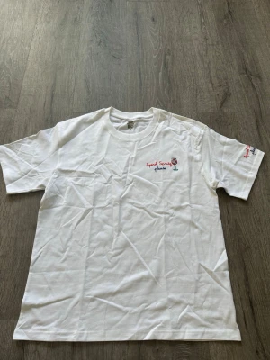 Saint Barth inspired Vit t-shirt med Aperol Spritz-brodyr - Saint Barth inspired  Vit t-shirt i bomull med broderad text 'Aperol Spritz please' och ett glas på bröstet samt ärmen. Klassisk passform och rund halsringning. Perfekt för dig som gillar snygga detaljer och vill sticka ut lite extra.