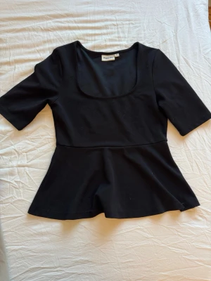 Svart topp med utsvängd midja Kappahl - Snygg svart topp från Kappahl med utsvängd midja och djup rundad urringning. Toppen har halvlånga ärmar och är tillverkad i ett mjukt, stretchigt material som sitter bekvämt. Perfekt att styla med jeans eller kjol.