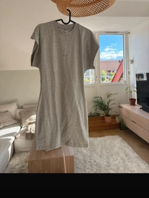 Grå t-shirtklänning från Avora - En enkel och stilren grå t-shirtklänning från Avora, Bianca Ingrossos märke! Klänningen har rund halsringning, korta ärmar och rak passform. Tillverkad i mjuk bomull för en bekväm känsla. Perfekt för en avslappnad look. Använd 1 gång