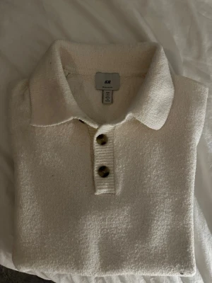 Vit kortärmad polotopp från H&M - Vit polotopp från H&M med korta ärmar och krage. Toppen har tre knappar framtill och är gjord i ett mjukt, stickat material. Bra skick och inga defekter. Köptes från hm för ungefär 350kr för några månader sedan. Säljs nu för 150kr. Passar perfekt nu till sommaren. Kontakta mig om du har några frågor.