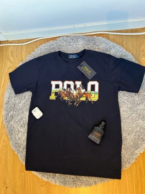  Polo t-shirt - T-shirt från med stort färgglatt POLO-tryck och polospelare på bröstet. Klassisk rund hals och korta ärmar. Perfekt för dig som gillar sportig och stilren streetwear.