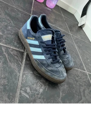 Adidas Spezial blå sneakers - Snygga Adidas Spezial sneakers i blå mocka med ljusblå detaljer och klassiska vita stripes på sidan. Gummisula och Adidas-logga på plösen samt insidan. Perfekta för dig som gillar retrostil och streetwear. Nästan helt oanvända