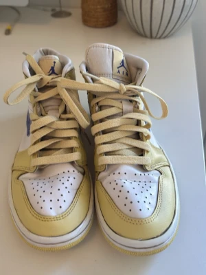 Nike Air Jordan 1 High Gul/Vit - Säljer ett par Nike Air Jordan 1 High sneakers i vitt och gult med blå swoosh. Klassisk high-top modell med perforerad tåbox och gula skosnören. Ovandelen är i läder och har ikoniska Air Jordan-detaljer på plösen och sidan, de är använda fler tals gånger men ändå i bra skick.