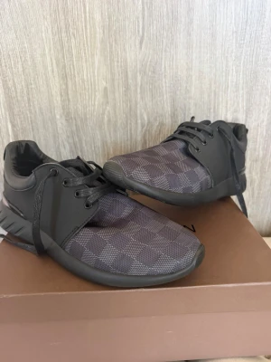Svarta sneakers - Snygga svarta sneakers med klassiskt rutmönster på ovandelen. Skorna har svarta snören, en chunky sula och detaljer i både textil och läder. Perfekta för dig som vill ha en stilren och exklusiv look.