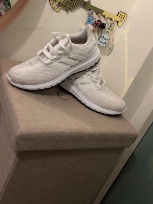 Vita Adidas ultra boost  - Snygga vita sneakers från Adidas med klassiska tre ränder på sidan. Skorna har ovandel i mesh för bra andningsförmåga och en vit sula med svart yttersula. Perfekta för dig som gillar stilrena och sportiga skor.