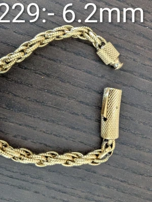 Guldfärgat titanstål armband unisex - Stilrent guldfärgat armband med flätad kedja och grov struktur. Armbandet har en robust, mönstrad skruvlåsdetalj som ger en cool och modern känsla. Perfekt accessoar för att lyfta din outfit med en touch av guld.