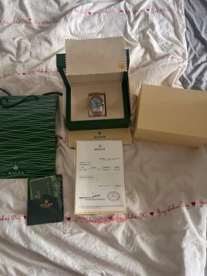 silverfärgad klocka - Säljer en stilren klocka i silverfärg med klassisk länkarmband och rund urtavla. Klockan levereras i originalbox med certifikat och tillbehör. Perfekt för dig som vill ha en exklusiv accessoar från ett ikoniskt märke.