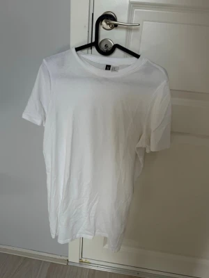 Vit t-shirt klänning från H&M - En klassisk vit t-shirtklänning från H&M i mjuk bomull. T-shirten har rund halsringning och korta ärmar, perfekt till alla outfits. Enkel och stilren design som passar till det mesta.