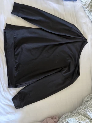 Svart off shoulder sweatshirt med rund hals - En enkel svart sweatshirt som är off shoulder på ena axeln med rund hals och långa ärmar. Tröjan har en avslappnad passform och är tillverkad i mjukt bomullsmaterial. Perfekt för en casual look och lätt att matcha med andra plagg.