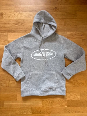 Grå hoodie med tryck framtill - Snygg grå hoodie med vit tryckt grafik på bröstet. Klassisk känguruficka och justerbar dragsko i huvan. Tillverkad i mjukt sweatshirtmaterial som är perfekt för chill dagar. Ribbade muddar vid ärmslut och nederkant för extra komfort. Står storlek M men sitter som S/XS