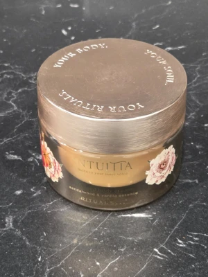 Rituals Intuita Body Cream - Ny och oanvänd!Lyxig body cream från Rituals i serien Intuita med doft av sandelträ och vanilj. Burken är brun med gulddetaljer och dekorerad med blommor. Innehåller naturliga ingredienser och ger huden en mjuk känsla. Perfekt för dig som vill unna dig något extra i din hudvårdsrutin.
