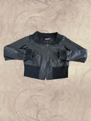 Svart skinnjacka - Snygg svart skinnjacka med bred ribbad mudd i midja, ärmslut och krage. Jackan har dragkedja framtill och två snedställda fickor. Kortare modell som ger en cool och modern look. Passar Storlek S/M. Har tappat en del nitar där bak men det är inget som inte går att fixa! Skriv för mått!  ♻️ Funky Fig ♻️ Skapat, återbrukat och utvalt med kärlek. Här får material, kläder och föremål nytt liv genom kreativitet, hantverk och hållbara val. Tack för att du stödjer småskaligt skapande. Get funky! ✨