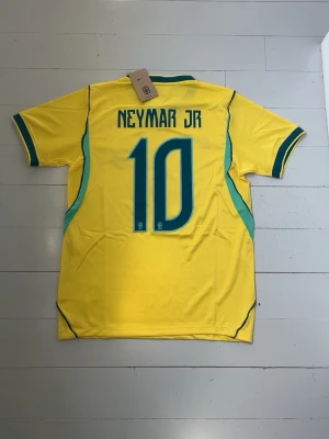 Brasilien Neymar 10 matchtröja Nike - Gul Brasilien fotbollströja från Nike med Neymar JR och nummer 10 på ryggen. Tröjan har gröna detaljer, CBF-emblem och BRASIL-text på bröstet. Tillverkad i lätt och ventilerande material, perfekt för träning eller match.