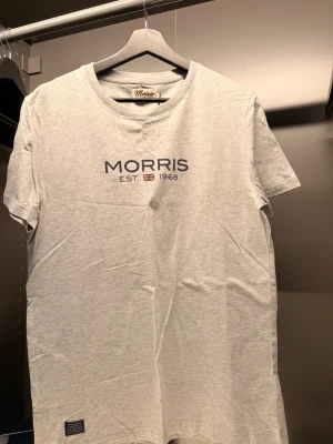 Morris - Snygg grå t-shirt från Morris med tryck 'MORRIS EST. 1968' och liten brittisk flagga på bröstet. Klassisk rund hals och korta ärmar. Tillverkad i mjuk bomull som känns skön mot huden. Perfekt till jeans eller shorts.