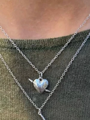 Halsband med hjärthänge i silver - Snyggt halsband i silverfärgad metall med ett hjärthänge som har en pil genom sig. Kedjan är tunn och stilren, perfekt för att ge en cool touch till din outfit. Hjärtat har en blank yta och pilen ger en edgy känsla.