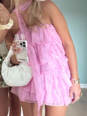 Rosa volangklänning  - Supersöt rosa kortklänning med flera lager volanger och axelbandslös design. Perfekt för dig som vill sticka ut! Klänningen är gjord i ett lätt, transparent tyg som ger en luftig känsla. Det är som en tajtklänning under, men super bekväm och lite stretchig! Passar nog XS och S