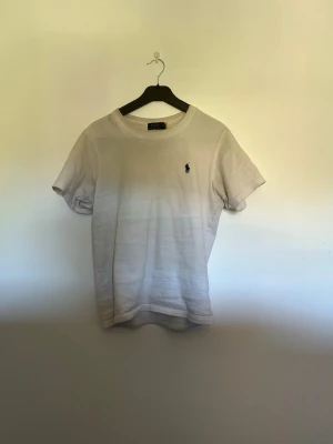 Vit t-shirt från Polo Ralph Lauren - Klassisk vit t-shirt från Polo Ralph Lauren med korta ärmar och den ikoniska broderade loggan på bröstet. Tillverkad i mjuk bomull för en skön känsla och enkel stil. Perfekt till jeans eller shorts för en clean look.