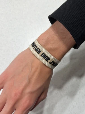 Beige armband - Snyggt beige armband med text i svart brodyr. Armbandet är gjort i vävt tyg med fransade kanter och har en stilren, trendig look som passar perfekt till din outfit.